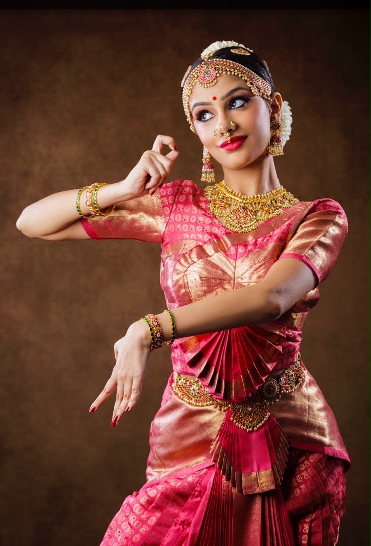 Ilesha Singh in rose-pink and gold silk, one hand raised in a delicate mudra, the other extended downward