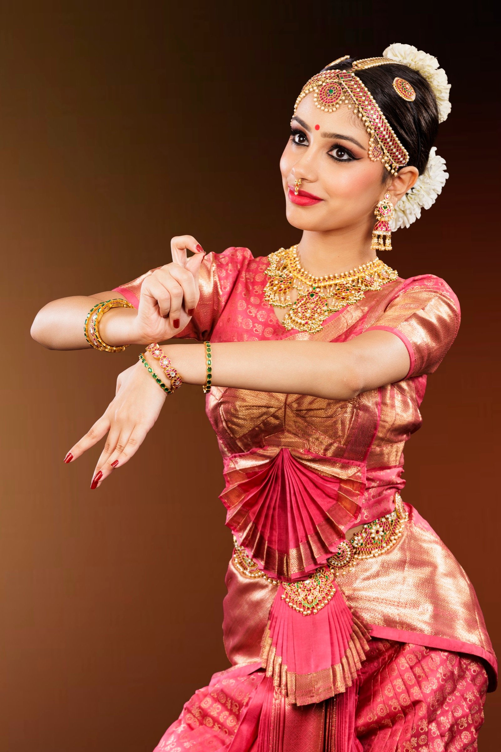 Ilesha in pink and gold Kanjivaram silk, hands crossed at the wrists with fingers fanned